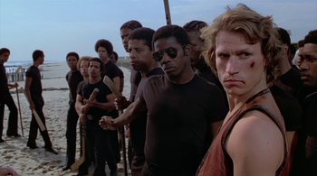 Movie still from “The Warriors” (1979), directed by Walter Hill – A group of men standing next to each other on a beach; Medium shot, Low angle