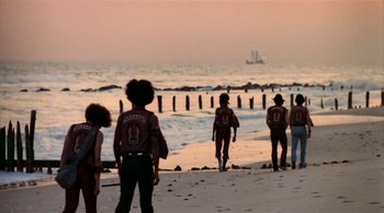 Movie still from “The Warriors” (1979), directed by Walter Hill – A group of people walking on the beach at sunset; Wide shot, Low angle