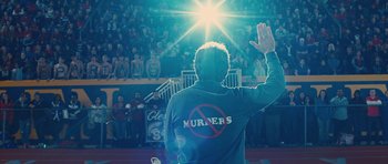 Movie still from “The Watch” (2012), directed by Akiva Schaffer – A man waves at a crowd of people in front of a stadium; Medium shot, Low angle