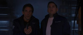 Movie still from “The Watch” (2012), directed by Akiva Schaffer – A couple of men standing next to each other holding a gun; Medium shot, Over the shoulder angle