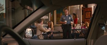 Movie still from “The Watch” (2012), directed by Akiva Schaffer – A police officer talking to two people sitting at an outdoor cafe; Medium shot, Over the shoulder angle