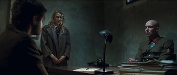 Movie still from “The Way Back” (2010), directed by Peter Weir – A woman standing in front of a desk with a lamp; Medium shot, Low angle