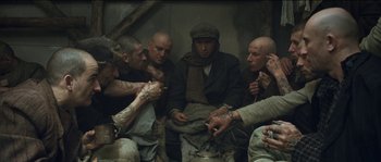 Movie still from “The Way Back” (2010), directed by Peter Weir – A group of men sitting around each other smoking cigarettes; Medium shot, High angle