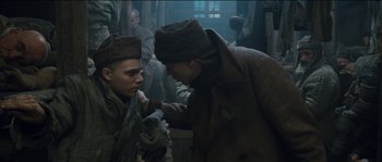 Movie still from “The Way Back” (2010), directed by Peter Weir – Two men in a room with a bunch of people; Medium shot, Low angle