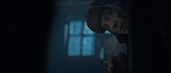 Movie still from “The Way Back” (2010), directed by Peter Weir – A man in a hood is smoking a cigarette in front of a window; Close Up shot, Low angle