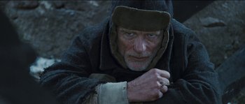 Movie still from “The Way Back” (2010), directed by Peter Weir – An old man wearing a hat is sitting on the ground; Close Up shot, High angle