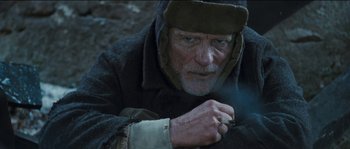 Movie still from “The Way Back” (2010), directed by Peter Weir – An old man with a beard is smoking a cigarette; Close Up shot, High angle