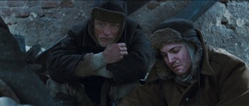 Movie still from “The Way Back” (2010), directed by Peter Weir – A man sitting next to another man in a hat; Medium shot, Low angle