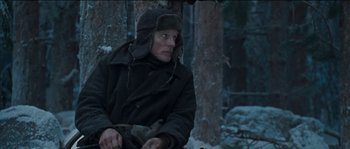 Movie still from “The Way Back” (2010), directed by Peter Weir – A man sitting in the snow next to a tree; Medium shot, Low angle