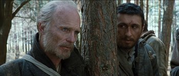 Movie still from “The Way Back” (2010), directed by Peter Weir – Two men standing next to a tree in the woods; Close Up shot, Over the shoulder angle