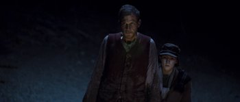 Movie still from “The Way Back” (2010), directed by Peter Weir – A man and a boy are standing in the dark; Medium shot, High angle