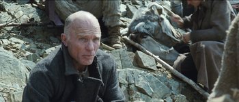 Movie still from “The Way Back” (2010), directed by Peter Weir – An older man sitting on the ground in front of rocks; Close Up shot, Low angle