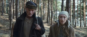 Movie still from “The Way Back” (2010), directed by Peter Weir – A man and a woman standing next to each other in the woods; Medium shot, Low angle