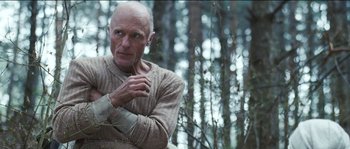 Movie still from “The Way Back” (2010), directed by Peter Weir – An older man wearing a sweater in the woods; Medium shot, Low angle