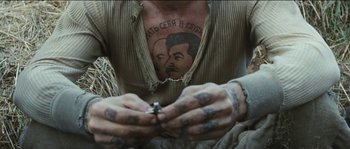 Movie still from “The Way Back” (2010), directed by Peter Weir – A man with a tattoo on his chest and hands; Close Up shot, Overhead angle