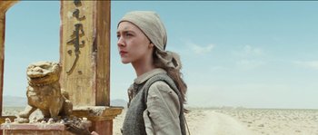 Movie still from “The Way Back” (2010), directed by Peter Weir – A woman in a head scarf standing next to a wooden post; Medium shot, Low angle