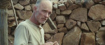 Movie still from “The Way Back” (2010), directed by Peter Weir – An older man holding a hammer near a pile of rocks; Close Up shot, Low angle