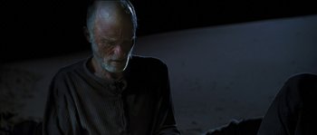 Movie still from “The Way Back” (2010), directed by Peter Weir – An older man sitting in the dark looking down; Medium shot, Over the shoulder angle