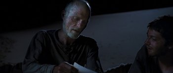 Movie still from “The Way Back” (2010), directed by Peter Weir – An older man is reading a paper in the dark; Close Up shot, Over the shoulder angle