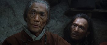 Movie still from “The Way Back” (2010), directed by Peter Weir – A man with long black hair wearing a brown shirt; Close Up shot, Low angle