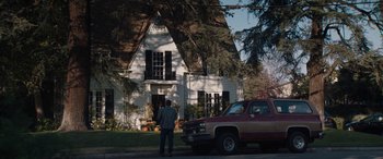 Movie still from “The Way Back” (2020), directed by Gavin O'Connor – A man standing in front of a house next to a red truck; Wide shot, Low angle