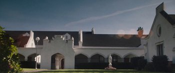 Movie still from “The Way Back” (2020), directed by Gavin O'Connor – A large white building with a statue of a woman in front of it; Extreme Wide shot, Low angle