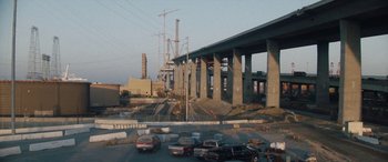 Movie still from “The Way Back” (2020), directed by Gavin O'Connor – Cars are parked on the side of a road near a bridge; Extreme Wide shot, High angle