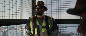 Movie still from “The Way Back” (2020), directed by Gavin O'Connor – A man in a hard hat and safety vest looking out of a window; Medium shot, Low angle