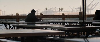 Movie still from “The Way Back” (2020), directed by Gavin O'Connor – A man sitting at a table in front of a chain link fence; Extreme Wide shot, Over the shoulder angle