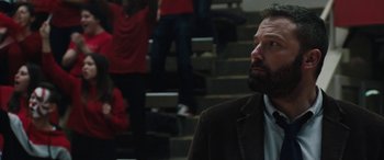 Movie still from “The Way Back” (2020), directed by Gavin O'Connor – A man in a suit and tie sitting in front of some stairs; Close Up shot, Over the shoulder angle