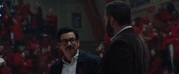 Movie still from “The Way Back” (2020), directed by Gavin O'Connor – Two men talking to each other in front of an audience; Medium shot, Over the shoulder angle