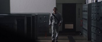 Movie still from “The Way Back” (2020), directed by Gavin O'Connor – A man wearing headphones walking down a hall way; Wide shot, Low angle