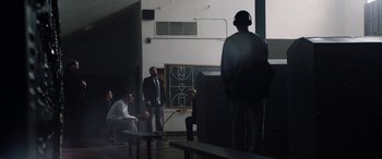 Movie still from “The Way Back” (2020), directed by Gavin O'Connor – A group of people in a room with a basketball court in the background; Wide shot, Low angle