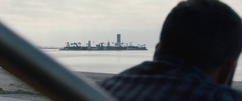 Movie still from “The Way Back” (2020), directed by Gavin O'Connor – A person sitting in front of a body of water; Extreme Wide shot, Over the shoulder angle