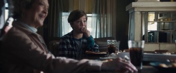 Movie still from “The Way Back” (2020), directed by Gavin O'Connor – A boy sitting at a table eating a piece of pizza; Medium shot, Over the shoulder angle