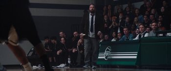 Movie still from “The Way Back” (2020), directed by Gavin O'Connor – A man standing in front of an audience holding a game controller; Wide shot, Over the shoulder angle