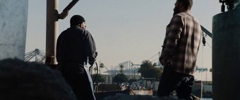 Movie still from “The Way Back” (2020), directed by Gavin O'Connor – A man standing next to another man holding a surfboard; Medium shot, Low angle
