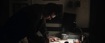 Movie still from “The Way Back” (2020), directed by Gavin O'Connor – A man writing on a piece of paper in front of a computer; Medium shot, Low angle