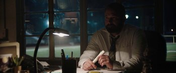 Movie still from “The Way Back” (2020), directed by Gavin O'Connor – A man sitting at a table holding a nintendo wii game controller; Medium shot, Low angle