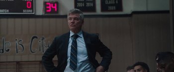 Movie still from “The Way Back” (2020), directed by Gavin O'Connor – A man in a suit and tie standing in front of a clock; Medium shot, Low angle
