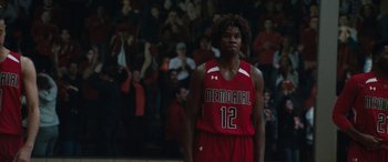 Movie still from “The Way Back” (2020), directed by Gavin O'Connor – A man in a red and white basketball uniform stands in front of a group of people; Medium shot, Low angle