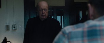Movie still from “The Way Back” (2020), directed by Gavin O'Connor – An older man wearing glasses and a black robe; Close Up shot, Over the shoulder angle