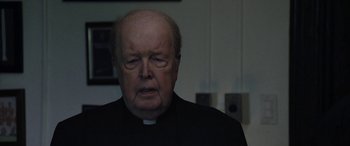 Movie still from “The Way Back” (2020), directed by Gavin O'Connor – An older man wearing a priest's outfit; Close Up shot, Over the shoulder angle