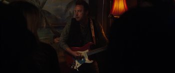 Movie still from “The Way Back” (2020), directed by Gavin O'Connor – A man holding a red guitar in a room; Medium shot, Over the shoulder angle
