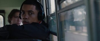 Movie still from “The Way Back” (2020), directed by Gavin O'Connor – A young man wearing headphones looking out of a bus window; Close Up shot, Low angle