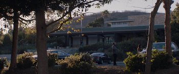 Movie still from “The Way Back” (2020), directed by Gavin O'Connor – A person standing on a sidewalk near a building; Extreme Wide shot, Low angle