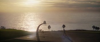 Movie still from “The Way Back” (2020), directed by Gavin O'Connor – A person is playing basketball on the beach at sunset; Extreme Wide shot, High angle