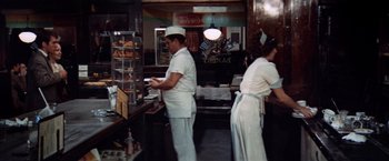 Movie still from “The Way We Were” (1973), directed by Sydney Pollack – Two men in white aprons working in a restaurant; Wide shot, High angle