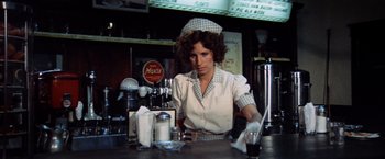 Movie still from “The Way We Were” (1973), directed by Sydney Pollack – A woman sitting at a counter in front of a soda machine; Medium shot, Low angle