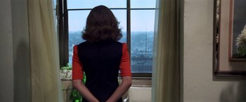 Movie still from “The Way We Were” (1973), directed by Sydney Pollack – A woman standing in front of a window looking out at a city; Medium shot, Over the shoulder angle